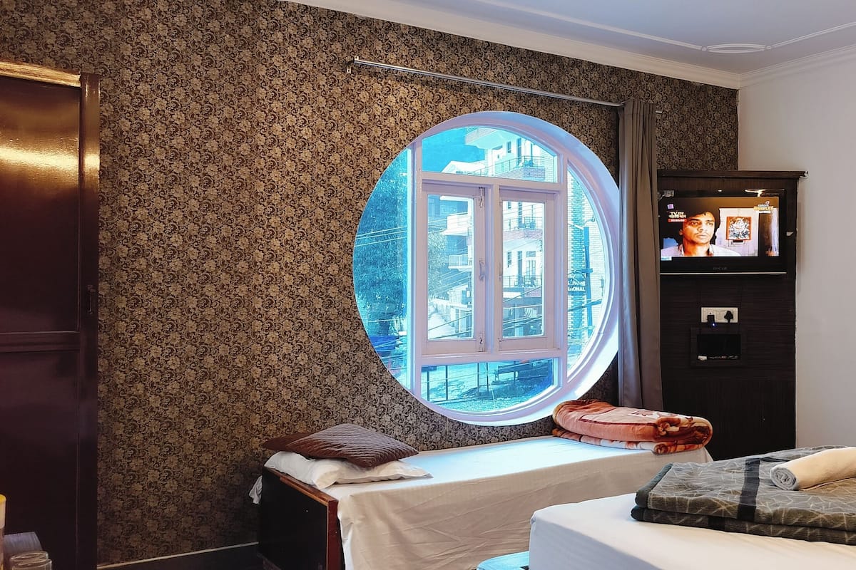 Quarto com janela redonda, cama com colcha estampada, mesa de cabeceira, guarda-roupa e televisão na parede.
