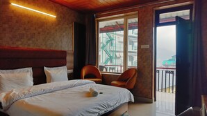 Ein Hotelzimmer mit Bett, zwei Stühlen, einem Fenster mit Blick auf Gebäude und einem Balkon.