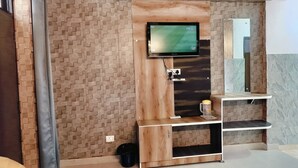 Ein Zimmer mit einer Ziegelwand, einem an der Wand befestigten Fernseher, einem Spiegel und einer Holzkabine mit Ablagefläche.
