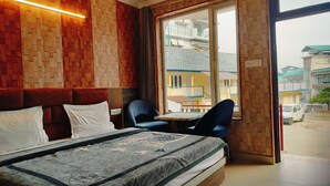 Ein Hotelzimmer mit einem Bett, einem kleinen Tisch, zwei Stühlen, einem Fenster mit Blick auf Gebäude und einer Wandgestaltung aus Holz.