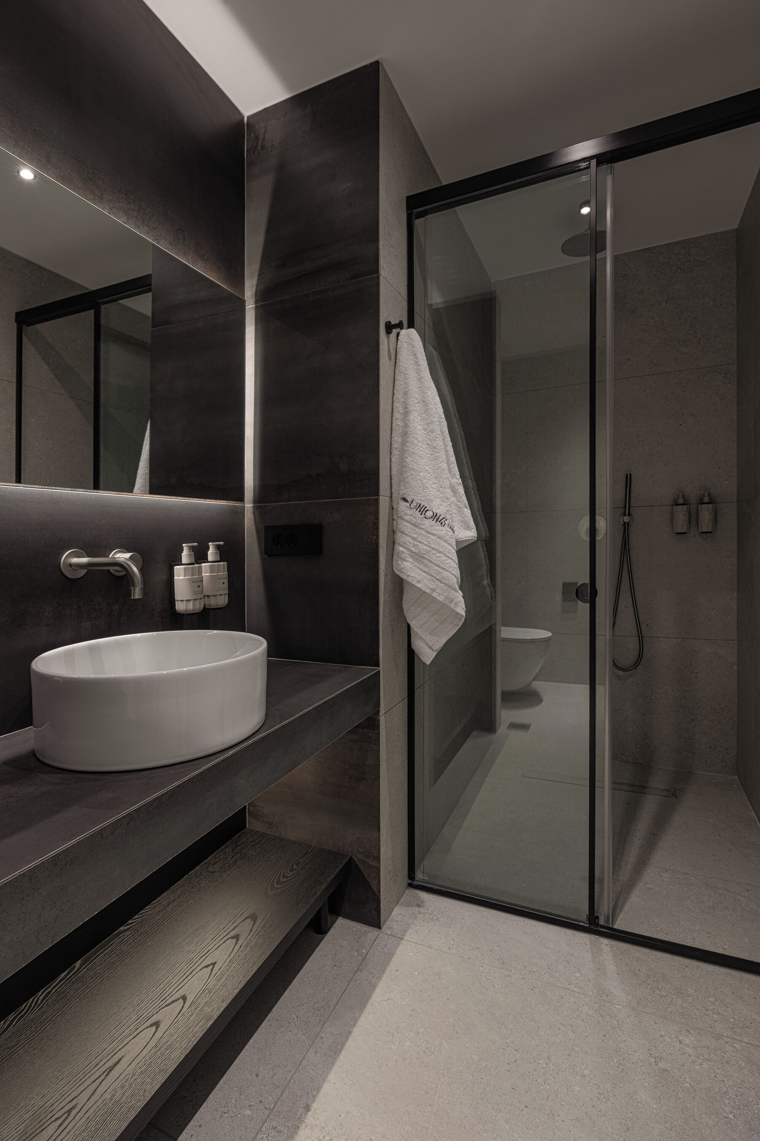 A modern bathroom with a large sink, a glass shower enclosure, and a towel hanging on the wall.