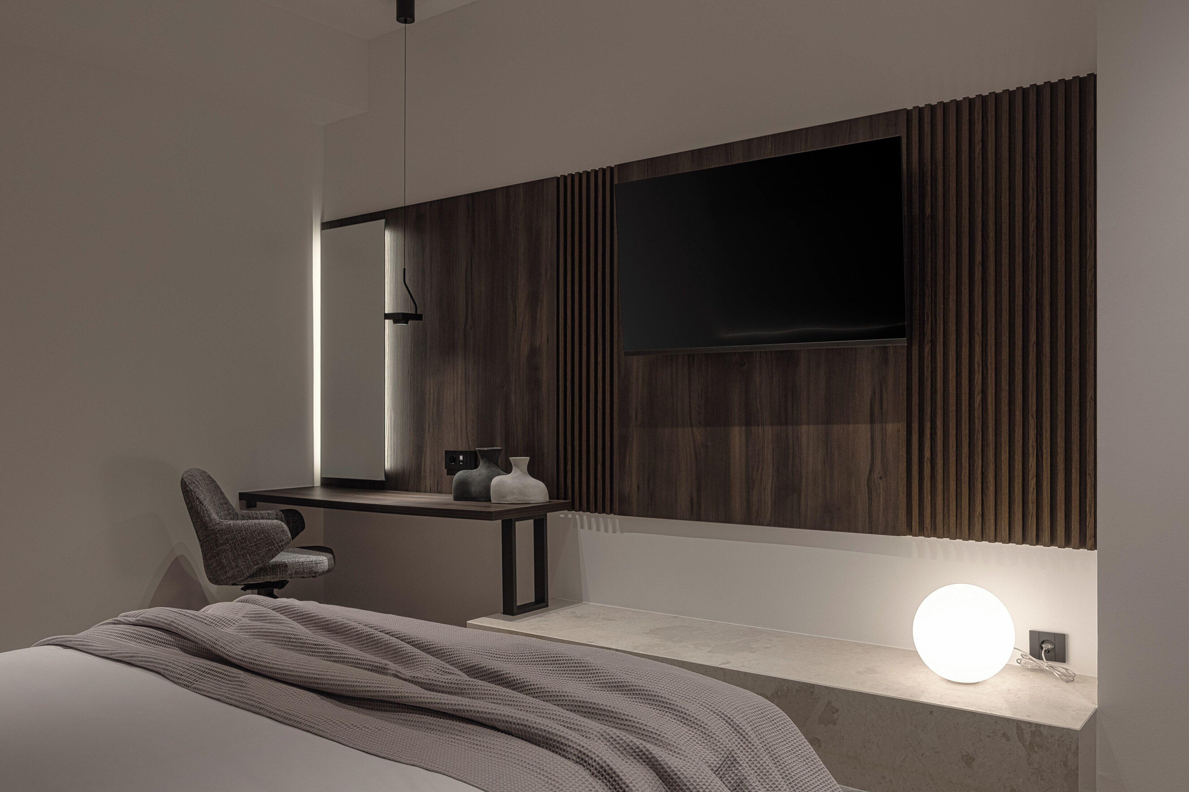 A modern bedroom with a bed, bedside table, chair, and a wall-mounted TV.