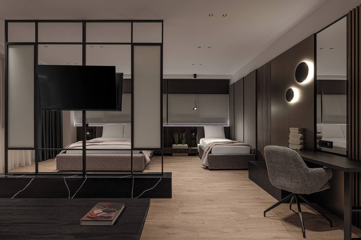 Una habitación de hotel moderna con un televisor de pantalla plana grande, dos camas, un escritorio con una silla y un espejo amplio.