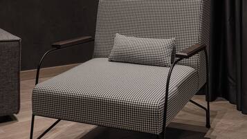 A modern chair with a checkered pattern, a side table, and a floor lamp in a room with dark curtains and a textured wall.