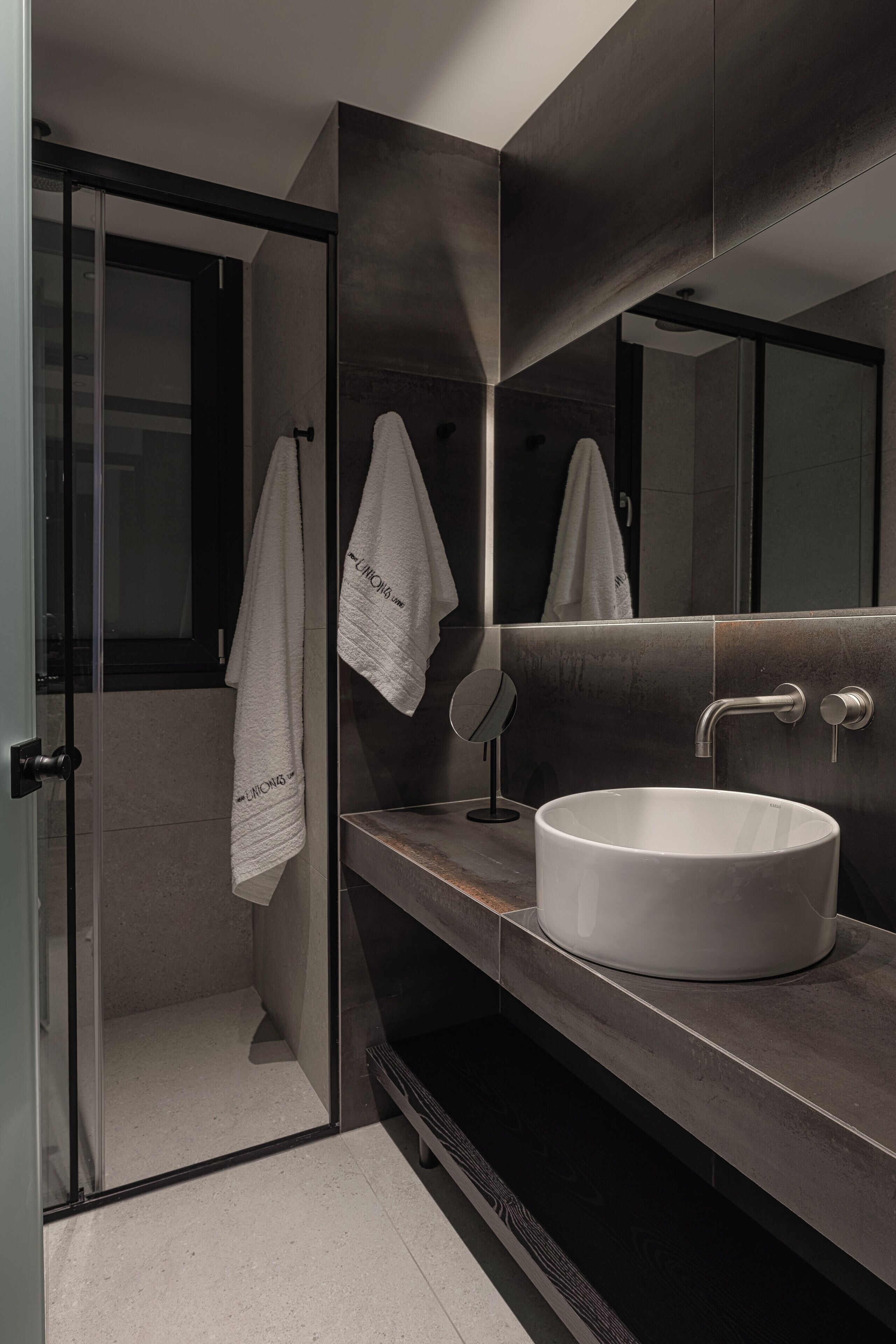 A modern bathroom with a glass shower enclosure, a white sink, and a large mirror.