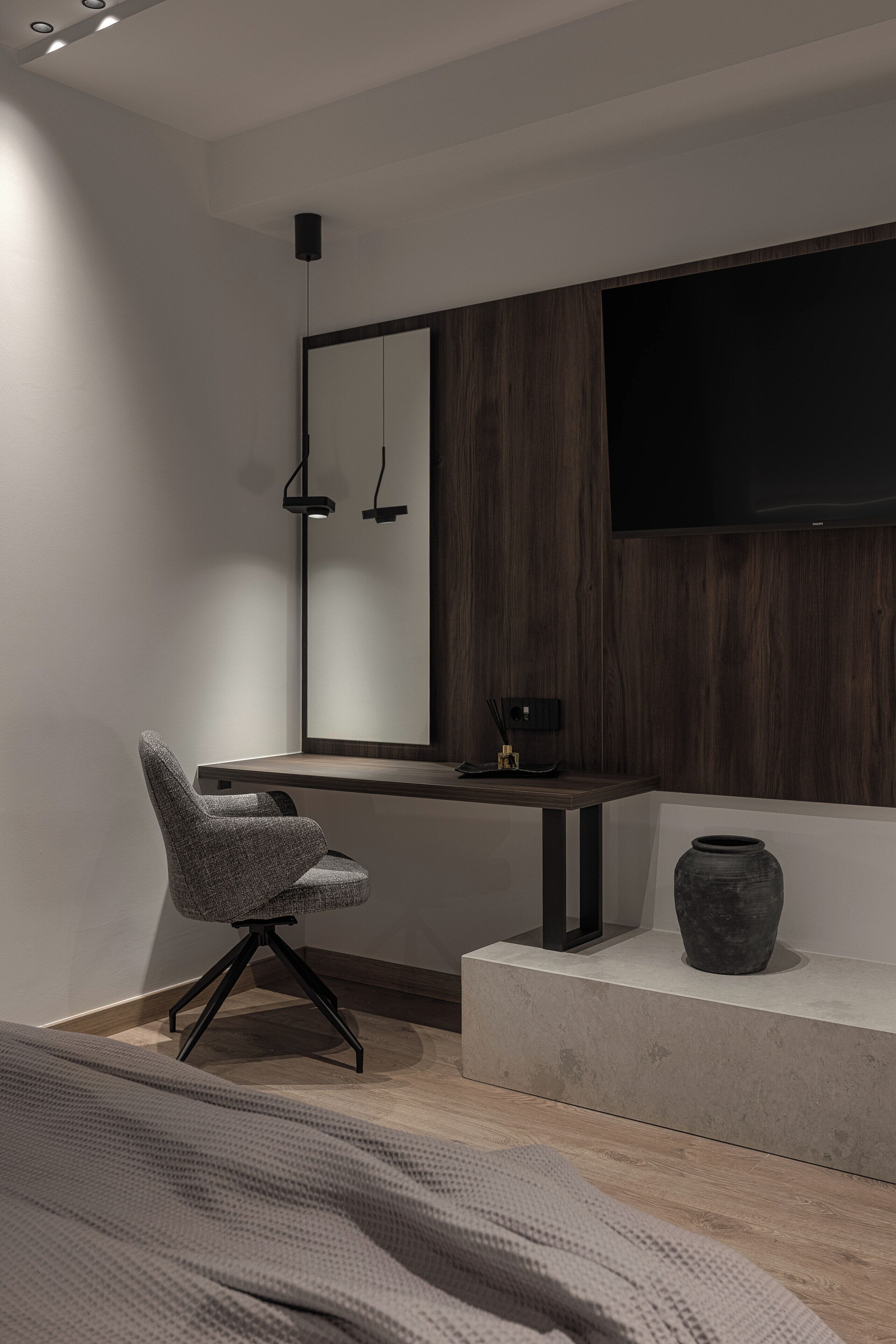 A modern room with a wooden accent wall, a large mirror, a flat-screen TV, a chair, a small table, and a vase.