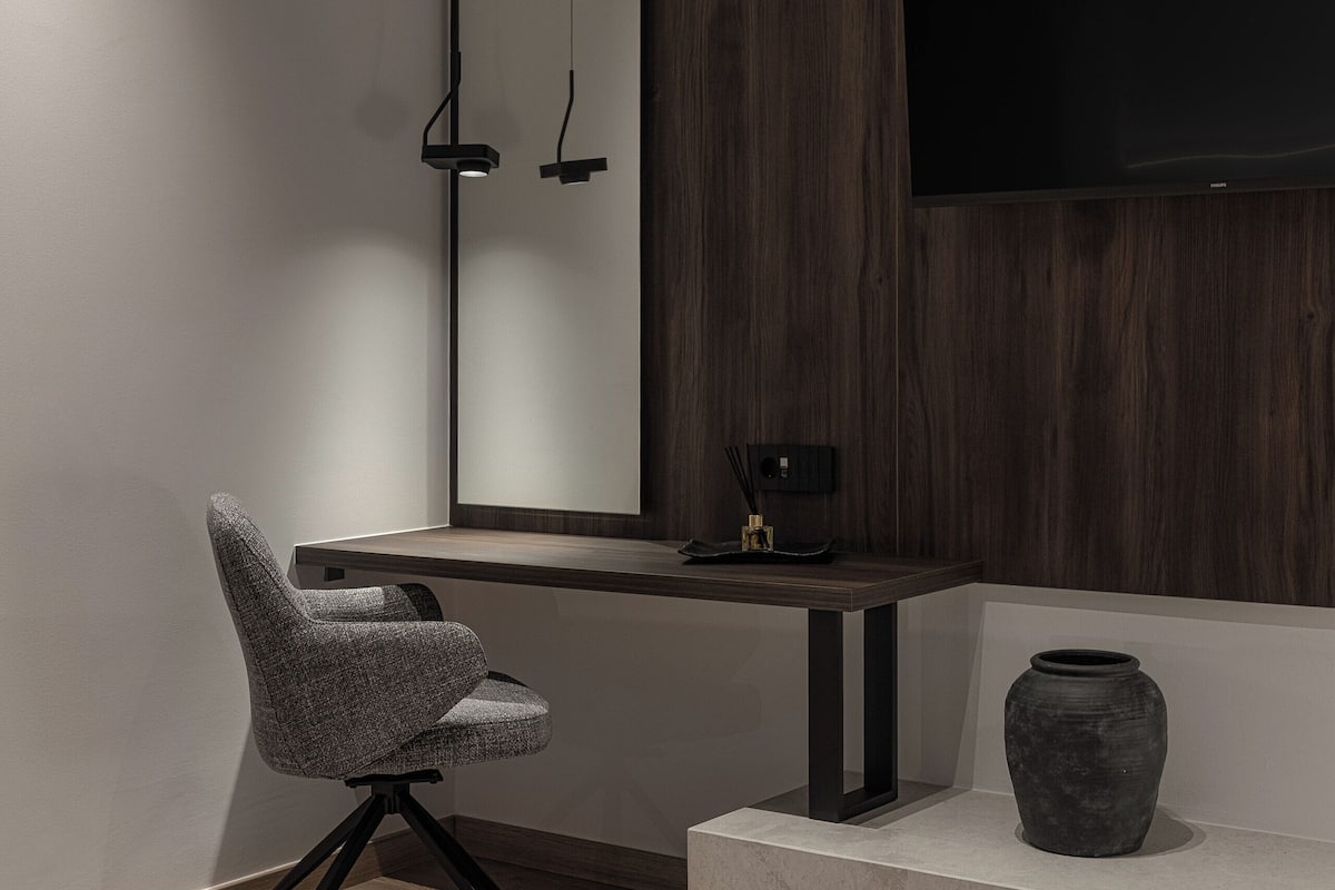 Una habitación moderna con un revestimiento de pared de madera, un espejo grande, un televisor de pantalla plana, una silla, una mesita y un florero.