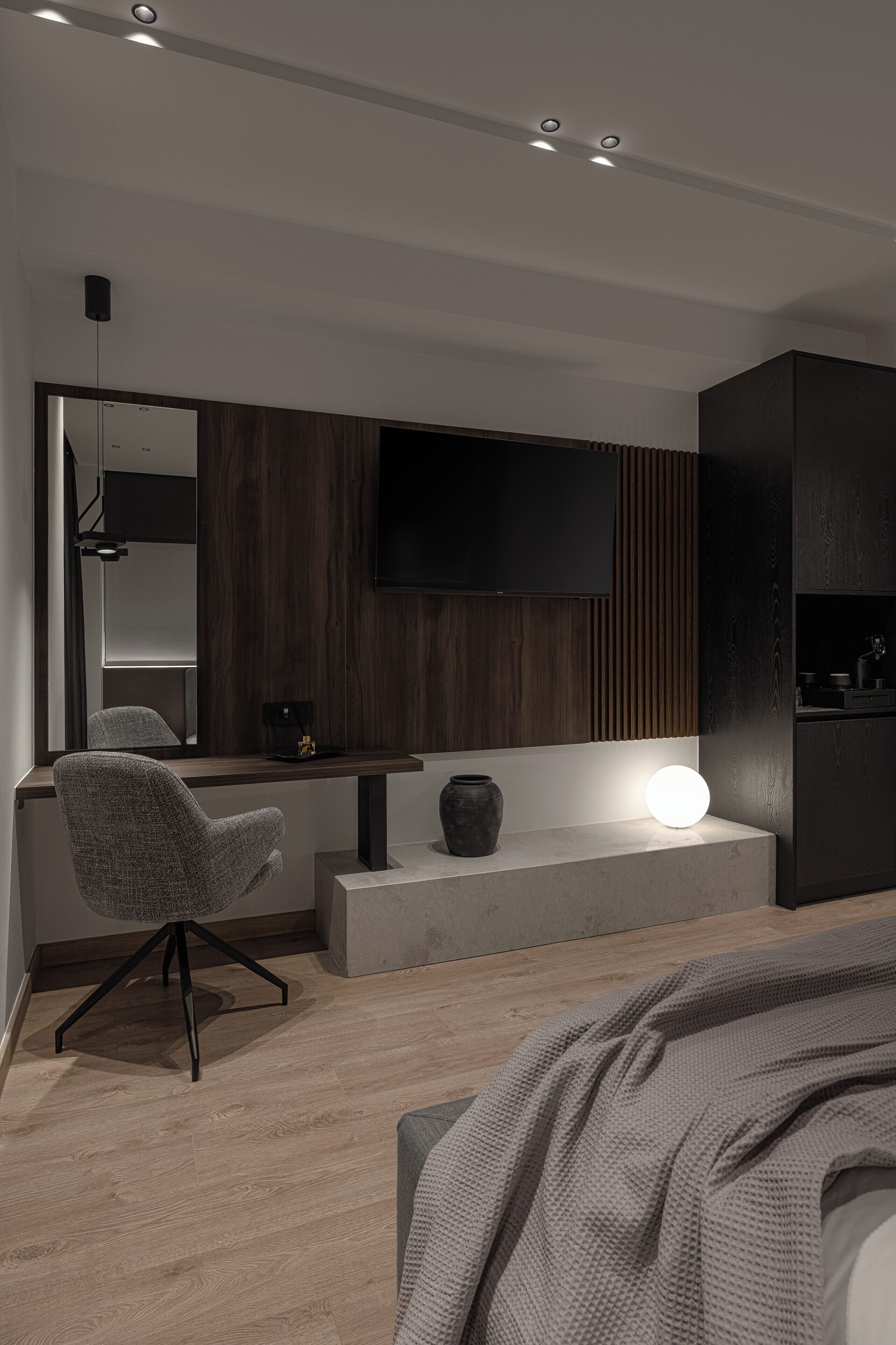 A modern bedroom with a bed, a desk, a chair, a TV, and a bedside table.