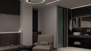 Ein modernes Interieur mit einem runden Tisch, einem Stuhl, einer Couch, einer Deckenleuchte und einem Badezimmer mit Waschbecken und Spiegel.