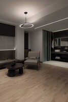 Un interior moderno con una mesa redonda, una silla, un sofá, una lámpara de techo y un baño con un lavabo y espejo.