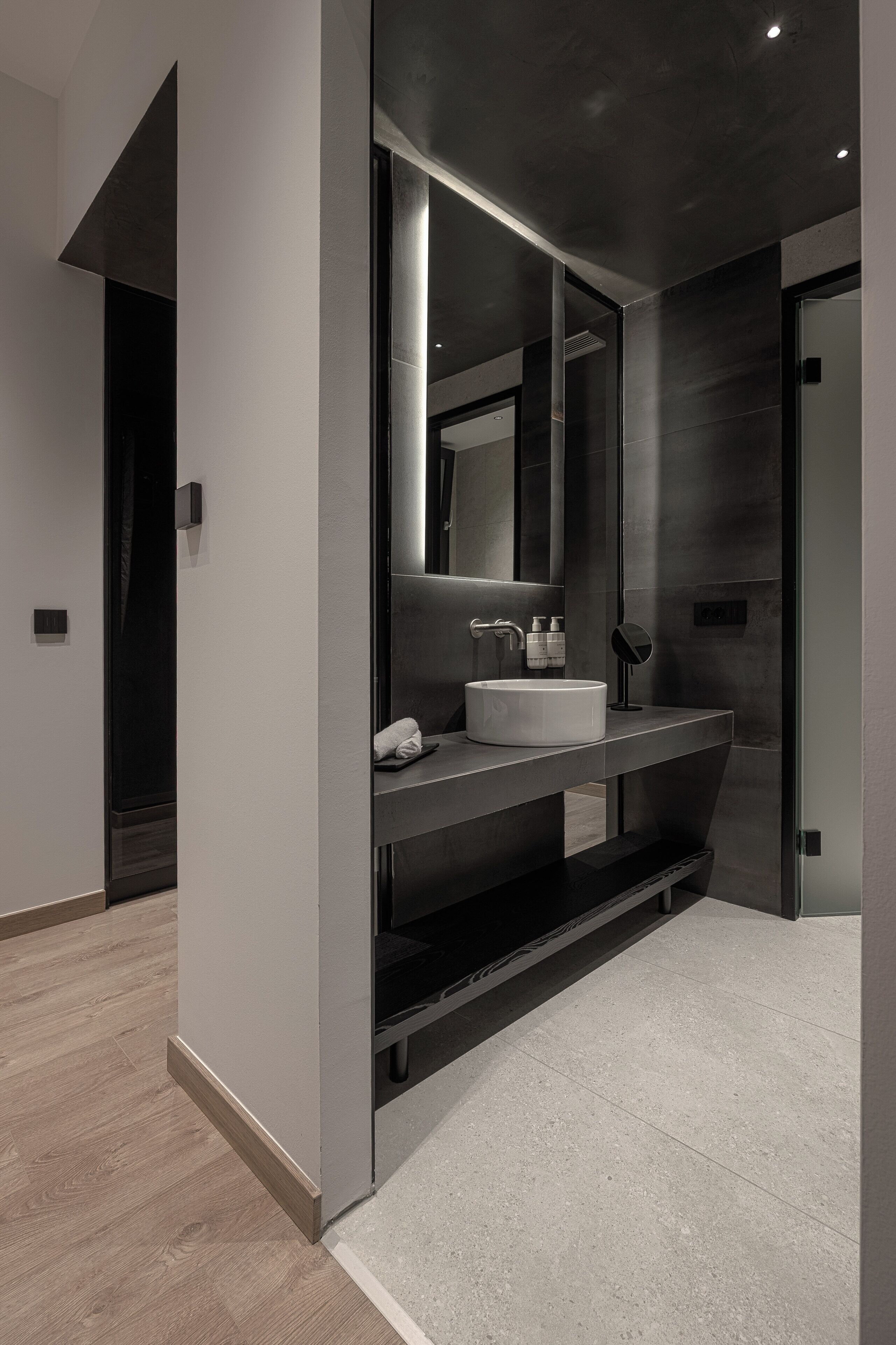 Un baño moderno con un espejo grande, un lavabo blanco y una encimera oscura.