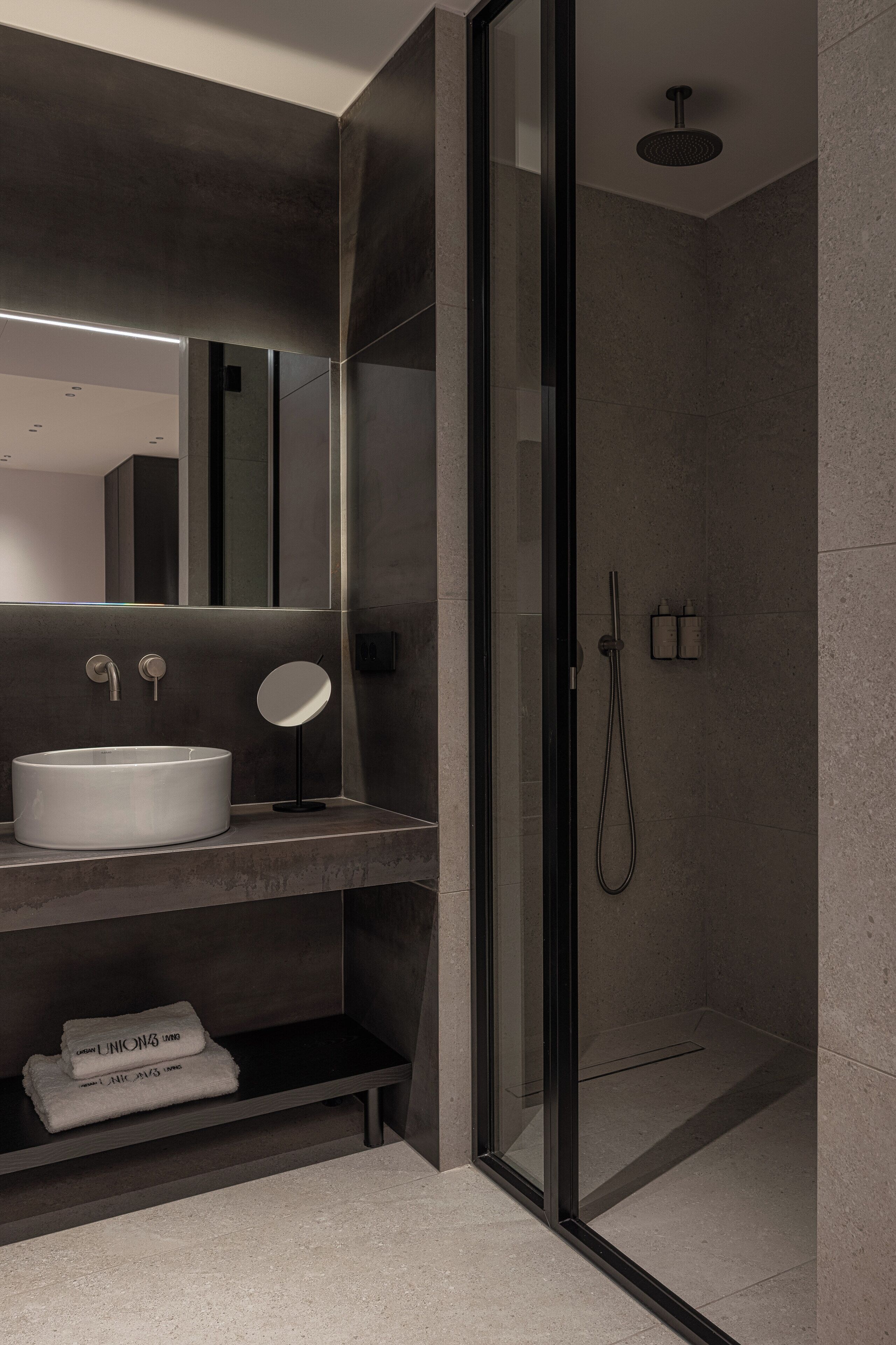 Un baño moderno con ducha de vidrio, espejo redondo y lavamanos blanco.