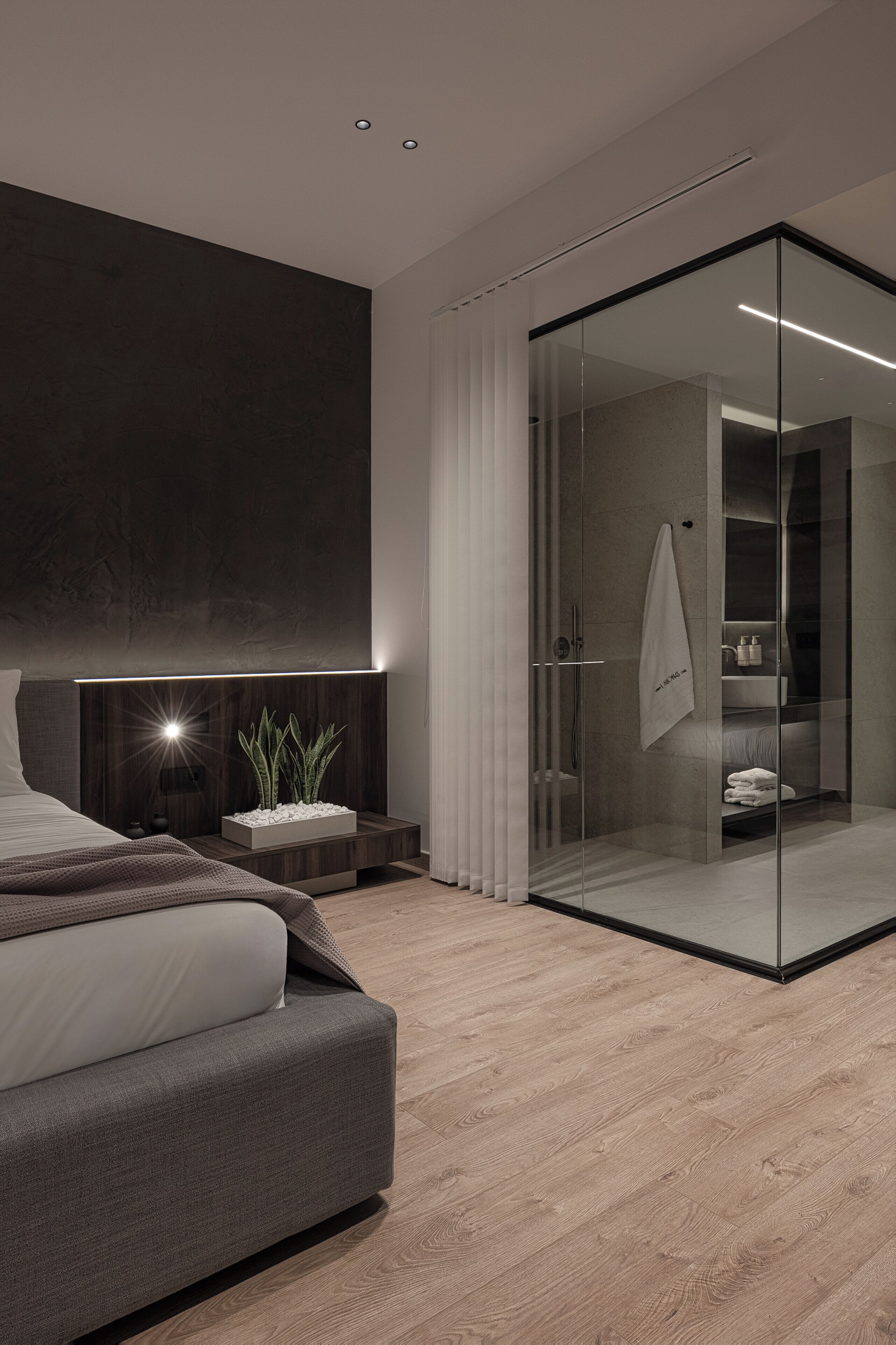 A modern bedroom with a bed, bedside table, and a glass-enclosed walk-in closet.