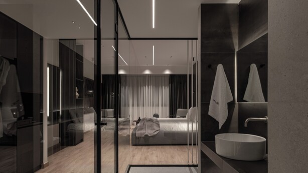 Ein modernes Hotelzimmer mit Glastrennwand, einem Bett, einem großen Spiegel, einem Waschbecken und einem Duschbereich.