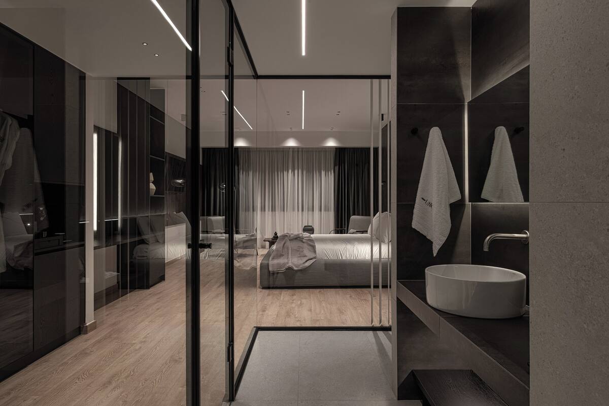 Una habitación de hotel moderna con separador de vidrio, cama, espejo grande, lavamanos y zona de ducha.
