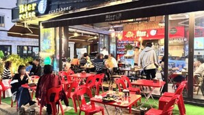 An outdoor dining area with red chairs and tables, a craft beer sign, and a storefront with a red awning. - Gangnam Style Village (Seoul)