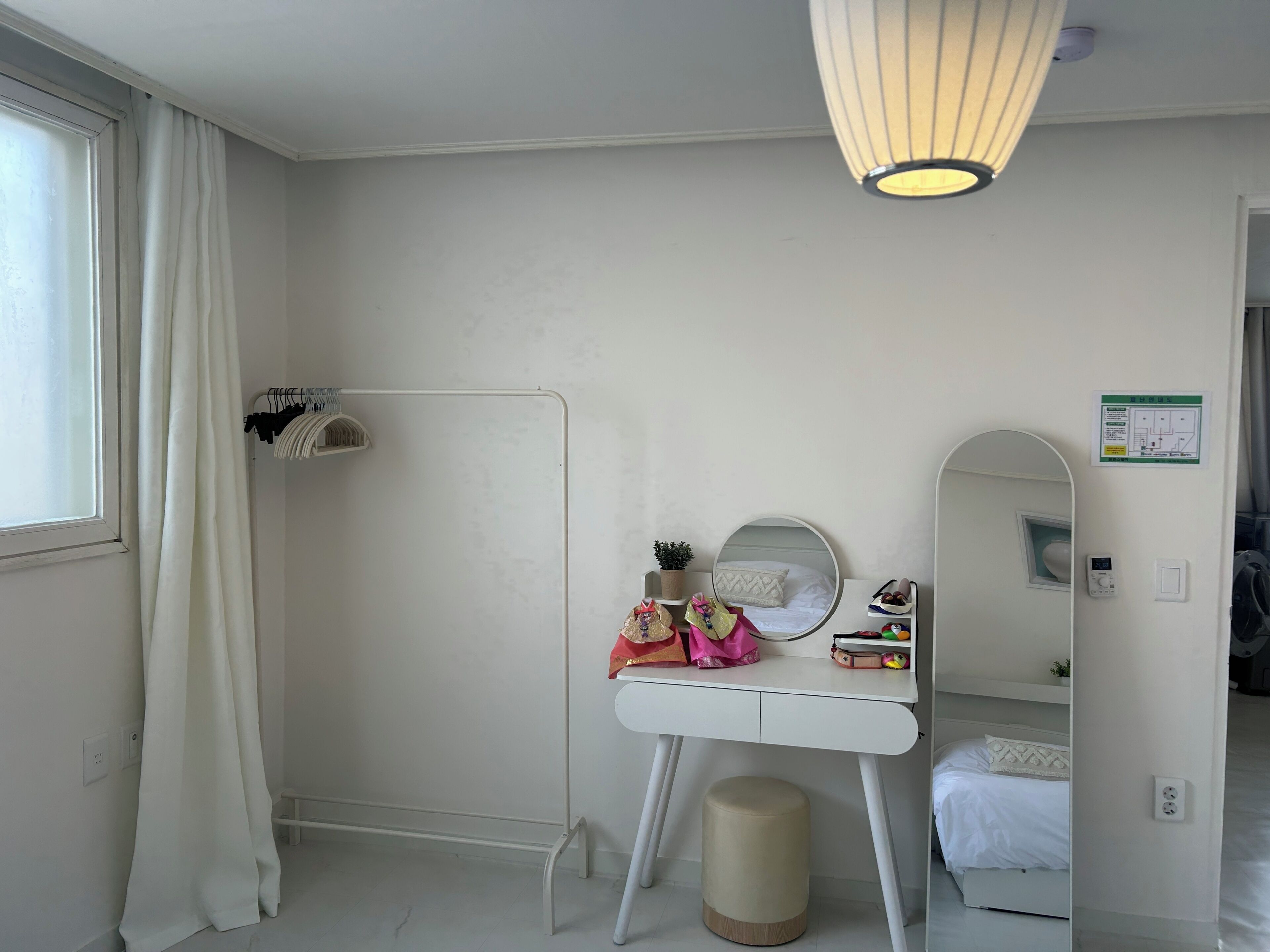 A bedroom with a bed, a bedside table with a mirror, a small stool, and a hanging light fixture.