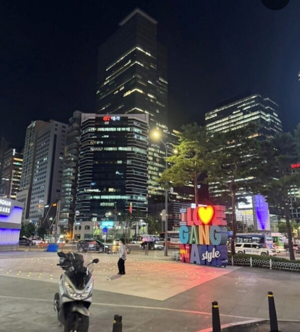A nighttime cityscape with illuminated skyscrapers and a prominent 'Bang Style' sign. - Gangnam Style Village (Seoul)