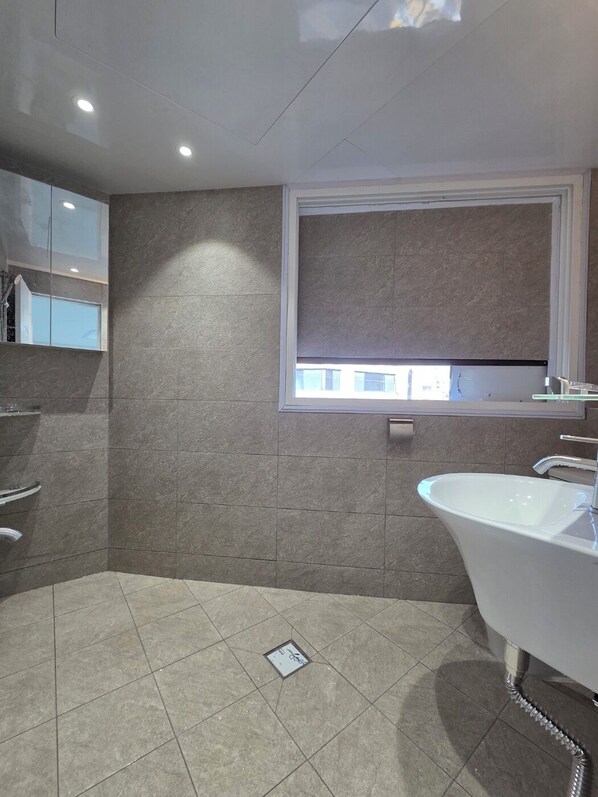 A modern bathroom with a freestanding bathtub, a window with a view, and a tiled floor. - Gangnam Style Village (Seoul)