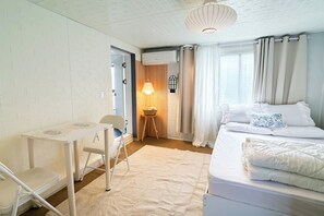 Un dormitorio con cama, escritorio, silla, lámpara y ventana con cortinas.