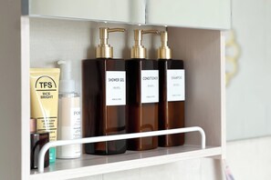 Un estante de baño con varios artículos de aseo, incluyendo una bolsita de arroz para iluminar, una botella de gel de ducha, una botella de acondicionador y una botella de champú.
