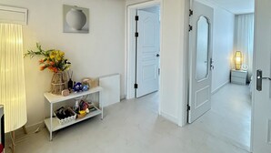 A hallway with a white floor, a white door, a white shelf with a vase of flowers, and a white lamp. - Gangnam Style Village (Seoul)