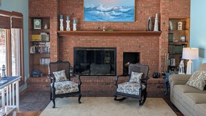 A living room with a brick fireplace, two armchairs, a sofa, a ceiling fan, and a bookshelf. - NEW!  The Lighthouse - Large Family-Friendly and Dog-Friendly Home on Big Platte Lake with Central A/C! (Beulah)
