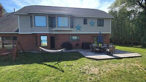 A two-story house with a patio area featuring a table and chairs, a hammock, and a swing set. - NEW!  The Lighthouse - Large Family-Friendly and Dog-Friendly Home on Big Platte Lake with Central A/C! (Beulah)
