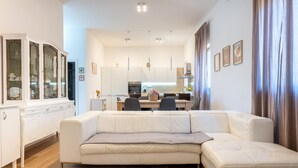Uma sala de estar moderna com um sofá seccional, uma área de jantar e uma cozinha ao fundo.