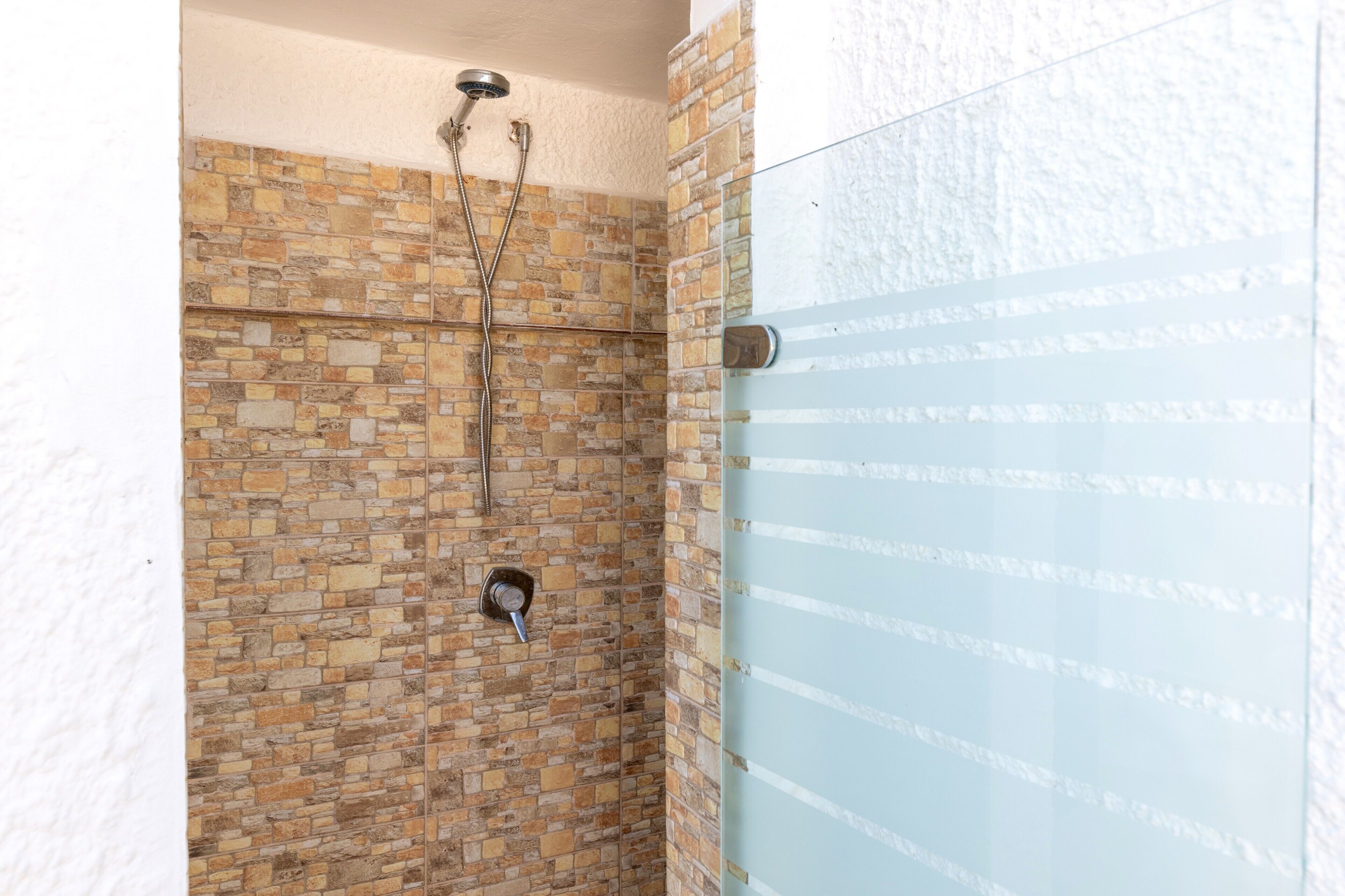 Eine Dusche mit Steinwand, Glastür und Duschkopf.