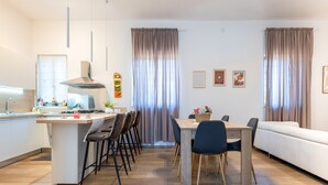Uma cozinha moderna com uma ilha central, banquetas, uma mesa de jantar com cadeiras e um sofá.
