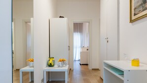 Um corredor com uma porta branca, uma mesa branca com flores amarelas, um armário branco e uma estante com uma caixa amarela.