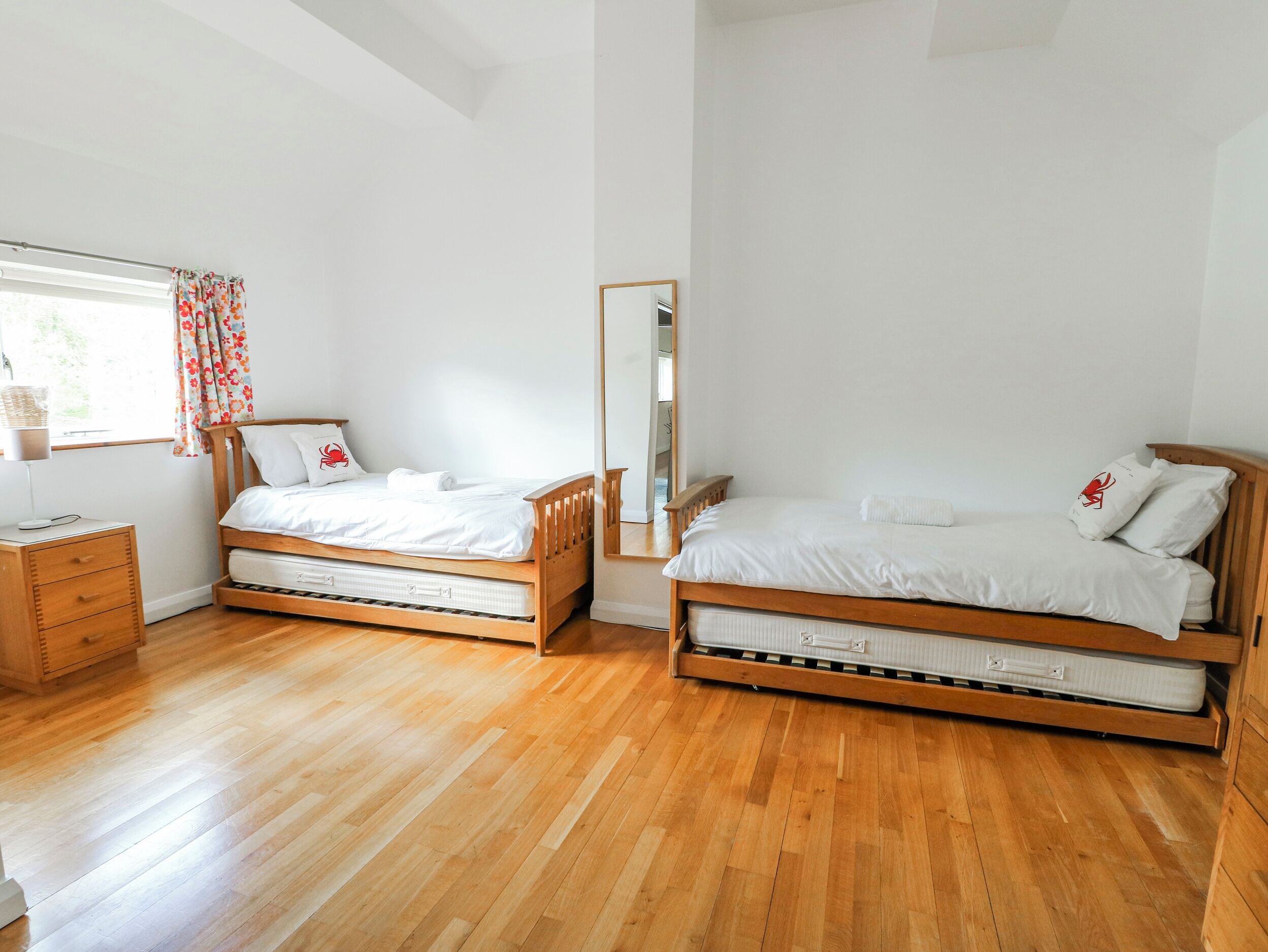 Une chambre à coucher avec deux lits en bois, une table de chevet, un miroir et une fenêtre avec des rideaux.