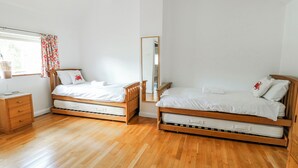 A bedroom with two wooden beds, a bedside table, a mirror, and a window with curtains.