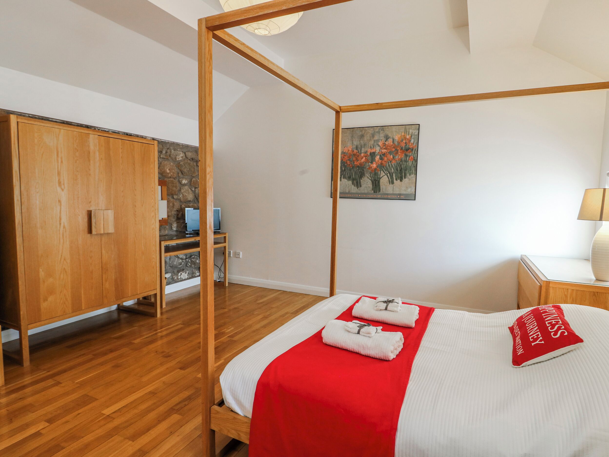 A bedroom with a four-poster bed, wooden wardrobe, and a desk with a computer.