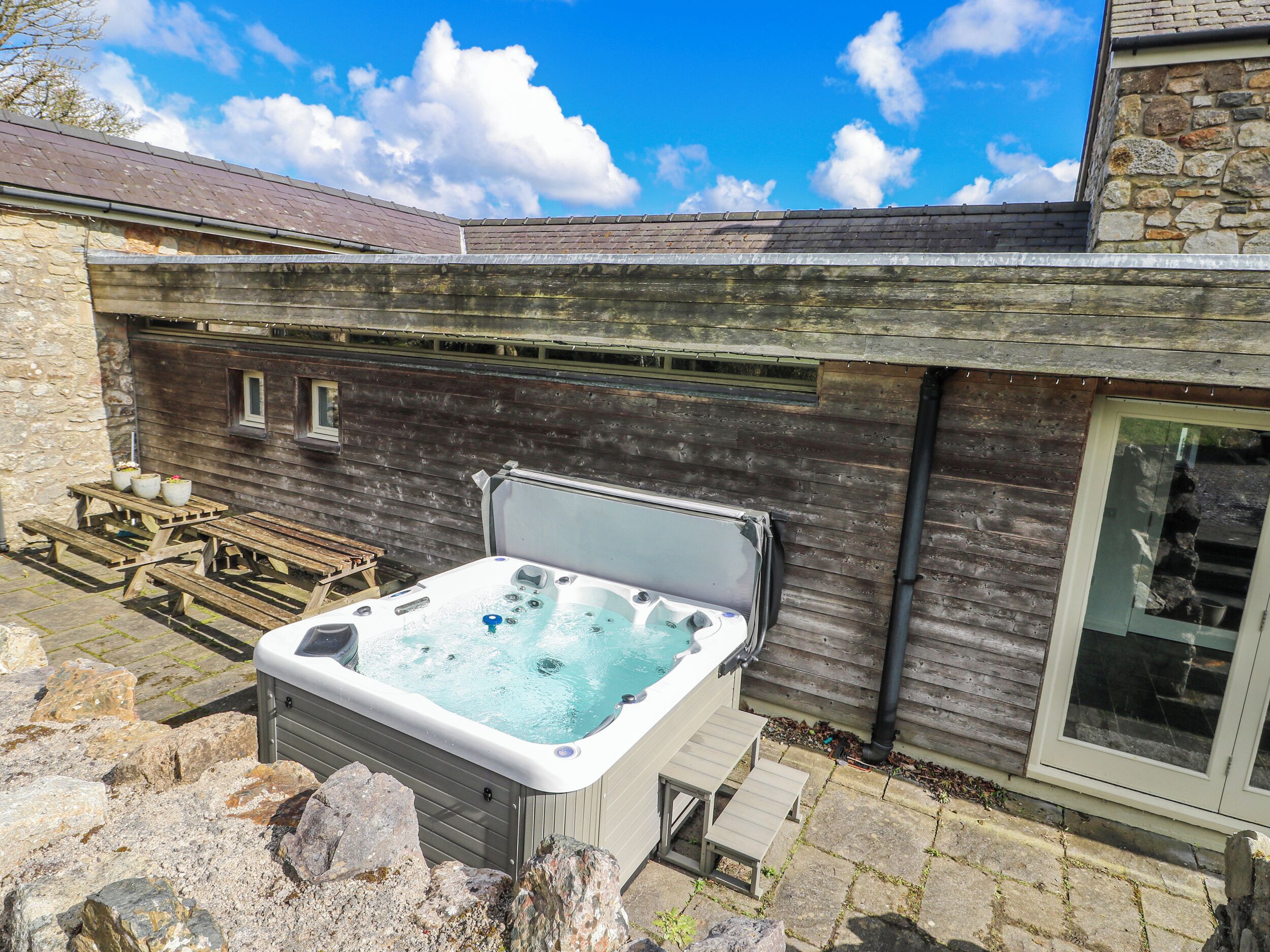 Un bain à remous dans un cadre extérieur rustique, avec des murs en pierre et des bancs en bois.