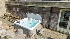 A hot tub in a rustic outdoor setting with stone walls and wooden benches.