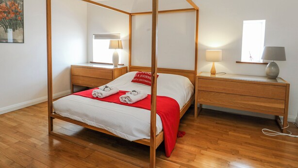 Ein Bett mit Baldachin, mit roter Bettdecke, ein Nachttisch mit Lampe, ein weiterer Nachttisch mit Lampe und ein Fenster mit Blick.