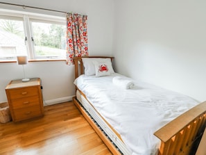 A bedroom with a wooden bed, a bedside table with a lamp, a window with curtains, and a wooden floor. - Too Hoots (Dulas)