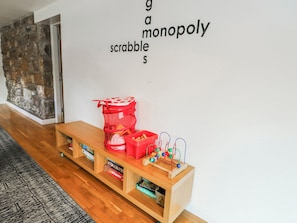 Una habitación con un banco de madera, una cesta de malla roja y un juego de Scrabble en la pared.