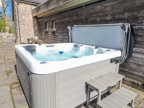 Un jacuzzi con revestimiento de madera, un banco integrado y una pared de piedra al fondo.