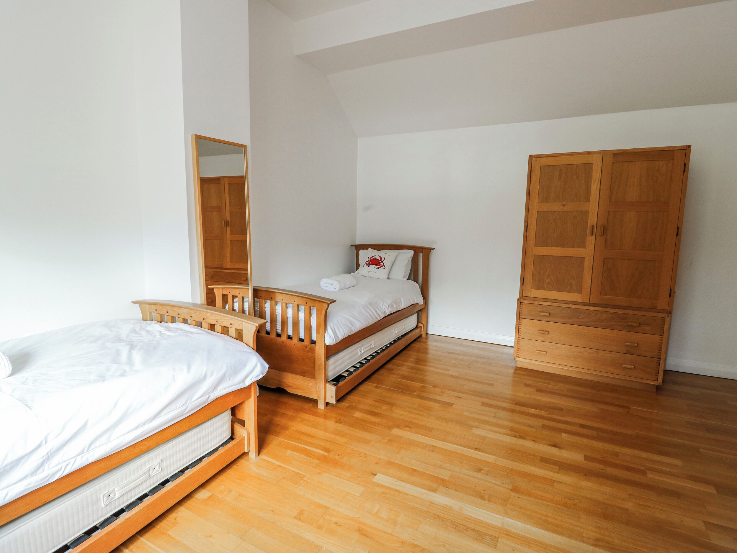 A bedroom with two wooden beds, a wooden wardrobe, and a mirror on the wall.