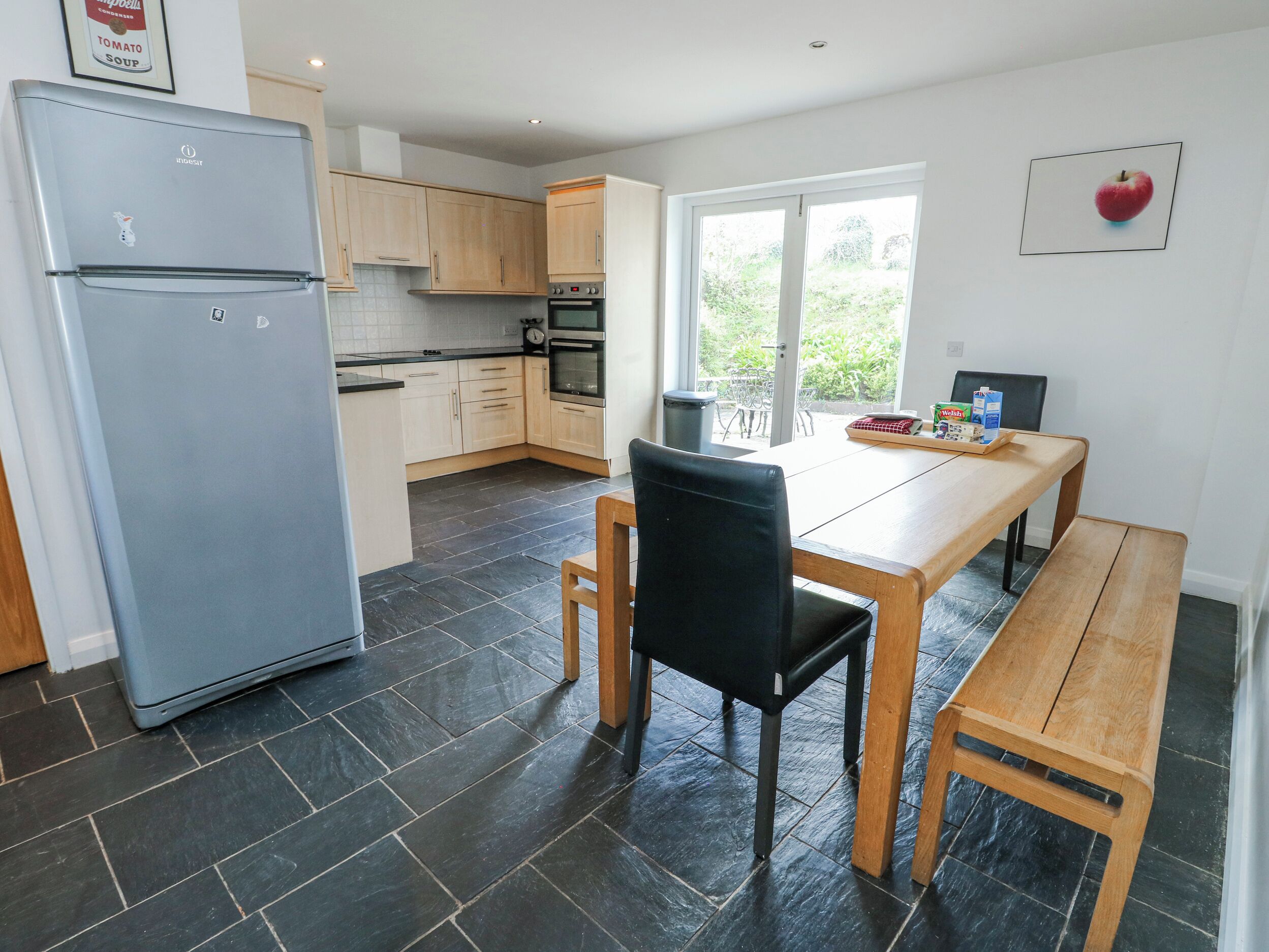 A modern kitchen with a refrigerator, oven, and dining area with a bench and chair.