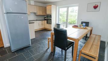 A modern kitchen with a refrigerator, oven, and dining area with a bench and chair.