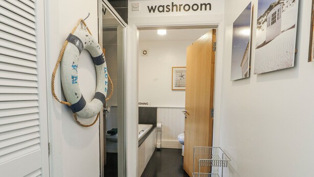 A hallway leading to a washroom with a lifebuoy on the wall, a metal rack, and a clock.