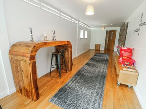 Un interior moderno con un escritorio de madera, una silla negra, un tapete gris estampado y un módulo de almacenamiento rojo.