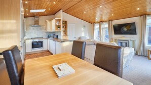 A modern kitchen with wooden ceiling, white cabinets, and a dining area with a wooden table and leather chairs. - Host Stay Mandarin Lodge (Malton)