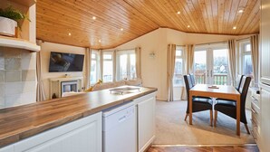 A modern kitchen with wooden ceiling, white cabinets, a built-in dishwasher, and a dining area with a table and chairs. - Host Stay Mandarin Lodge (Malton)