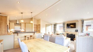 A modern kitchen with wooden cabinets, a dining area with a wooden table and chairs, a living room with a sofa and a fireplace, and a TV mounted on the wall. - Host Stay Little Gem Lodge (Malton)