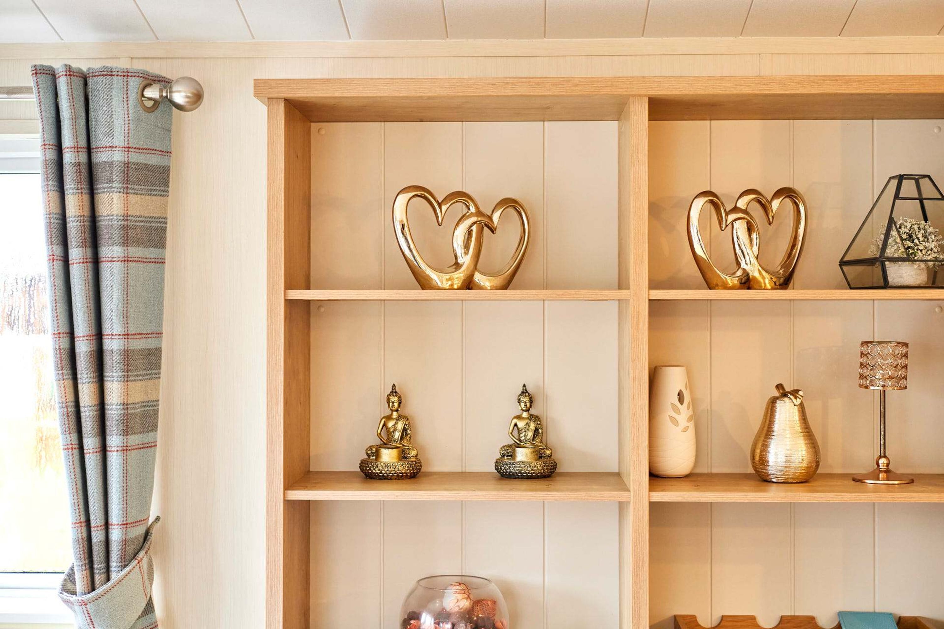 Une étagère en bois ornée d’objets décoratifs, notamment des objets en forme de cœur dorés, des statues de Bouddha, un vase en verre et une lampe.